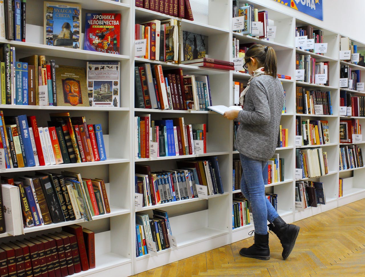 The Art of Drawing Readers In: Your attractive post title goes here A young woman stands reading a book in a well-stocked library.