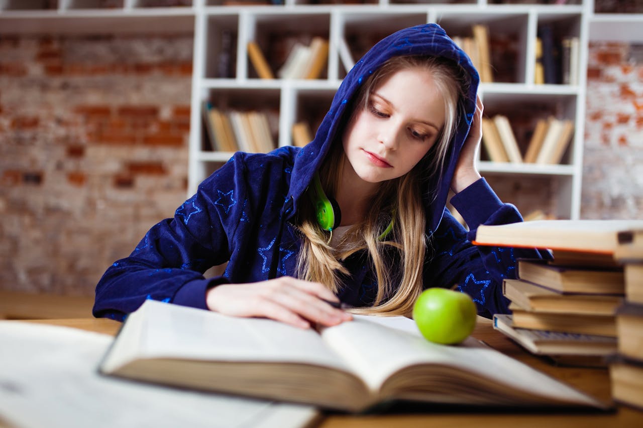 Mastering the First Impression: Your intriguing post title goes here Teenage girl in blue hood reads in library, headphones and apple by her side.